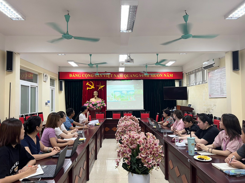 A group of people sitting at long tables in a room with a screenDescription automatically generated