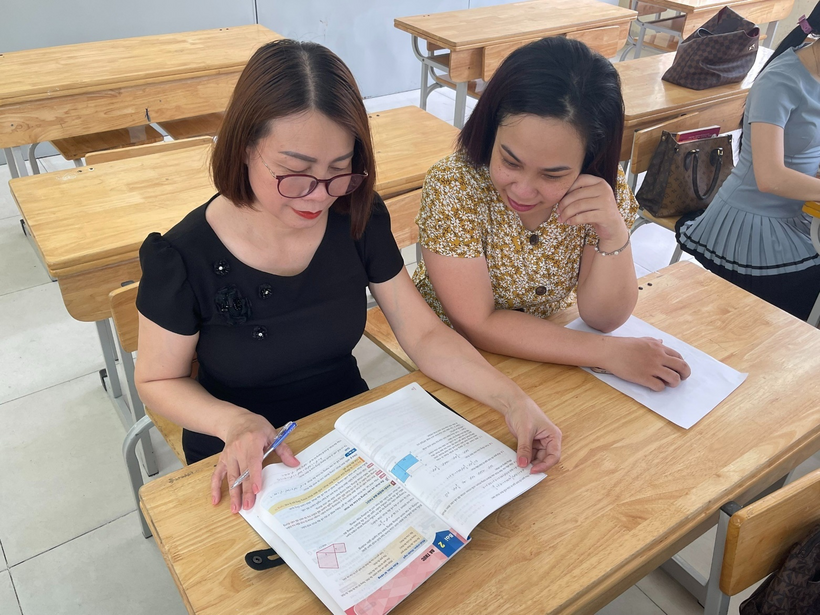 Two women sitting at a desk looking at a bookDescription automatically generated
