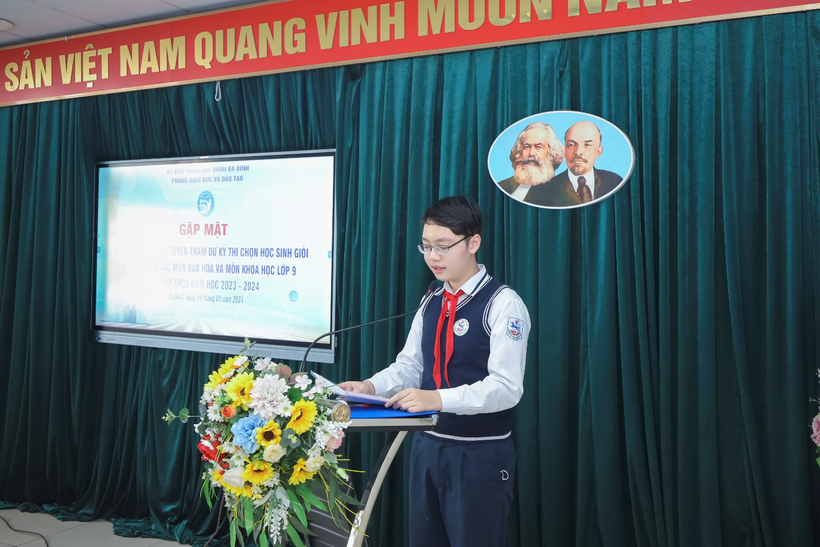 A person standing at a podium with a screen and flowersDescription automatically generated