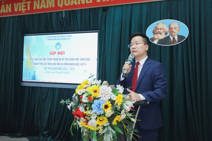 A person standing at a podium with a microphone and flowersDescription automatically generated