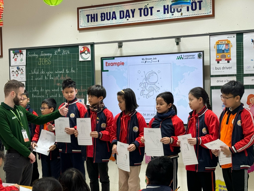 A group of children holding papers in a classroomDescription automatically generated