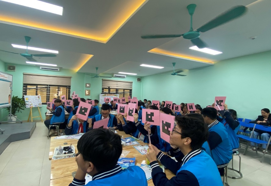 A group of people sitting at a table holding up pink signsDescription automatically generated